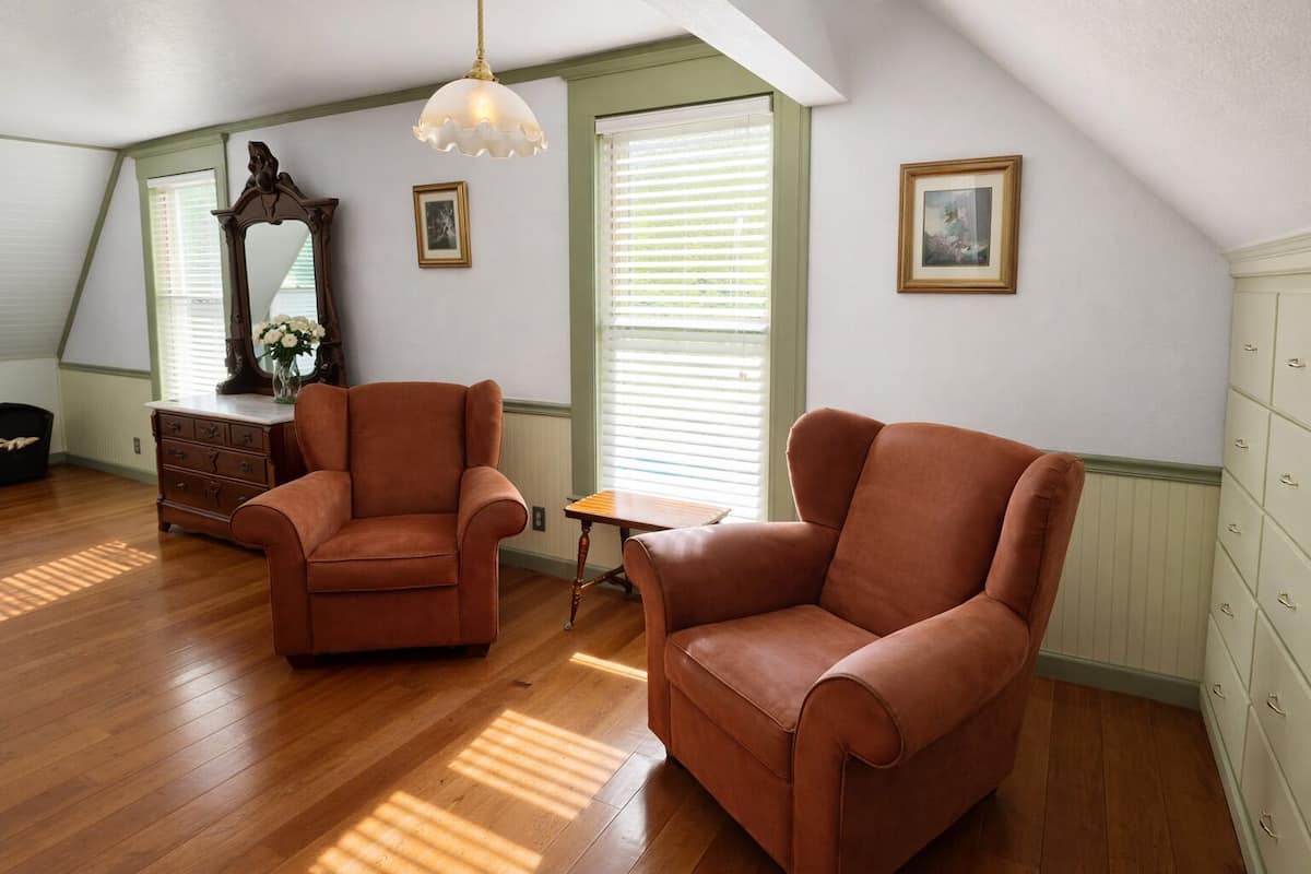 A room with two brown leather armchairs, a wooden dresser, a small table, a mirror, and a hanging light fixture.