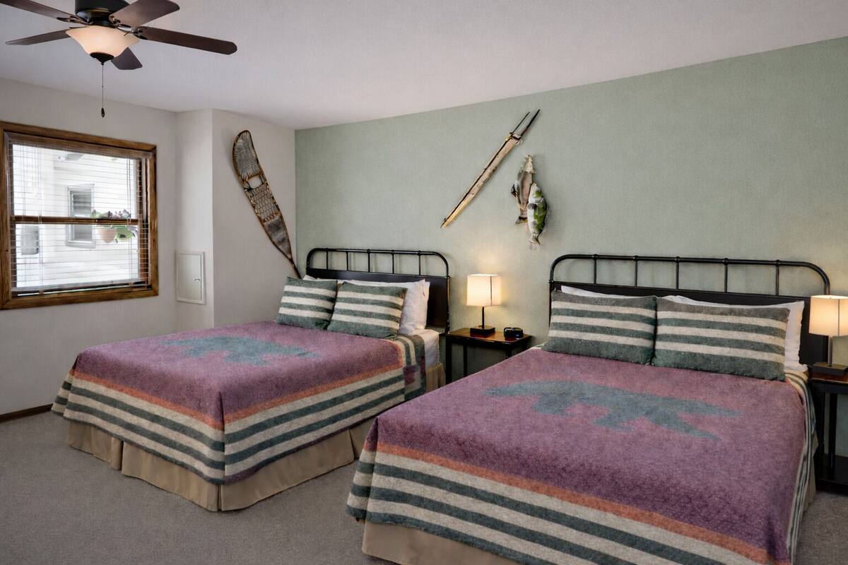A bedroom with two beds, a ceiling fan, a window, and wall decorations.