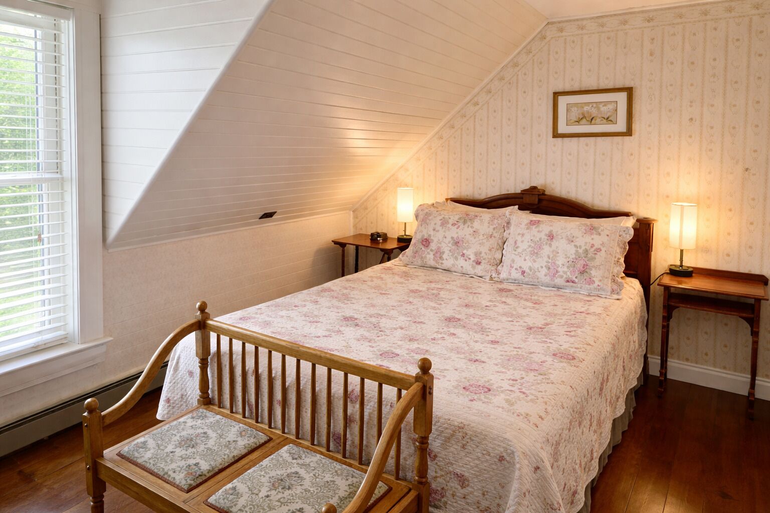Une chambre avec un plafond en pente, un cadre de lit en bois, une table de chevet et une chaise.