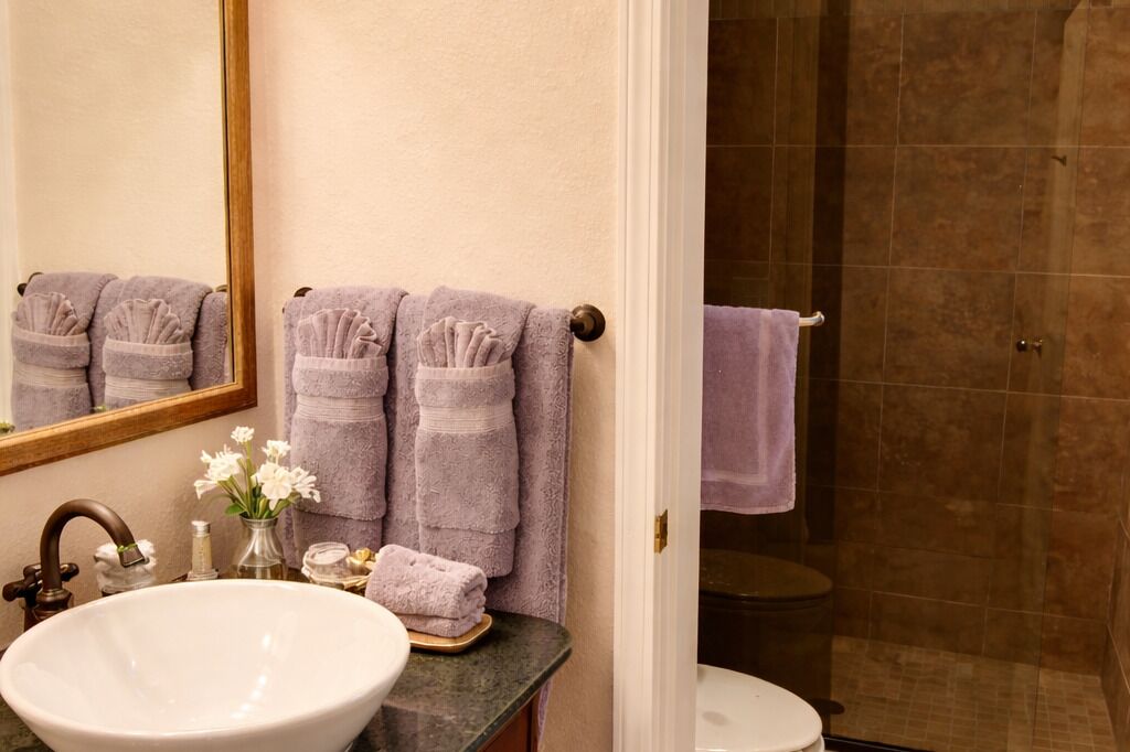 A bathroom with a sink, mirror, towels, and a shower area.