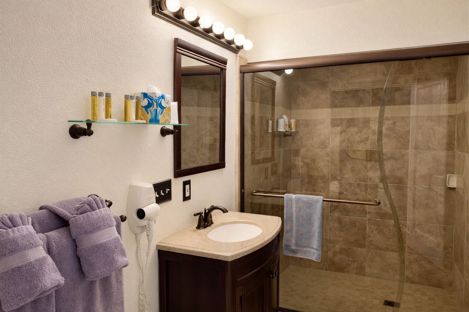 Un baño con ducha de vidrio, lavabo con espejo y toallas.