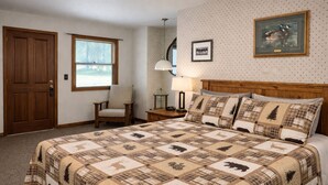 Une chambre à coucher avec un grand lit, une tête de lit en bois, une chaise, une table de chevet, une lampe et une fenêtre avec des stores.