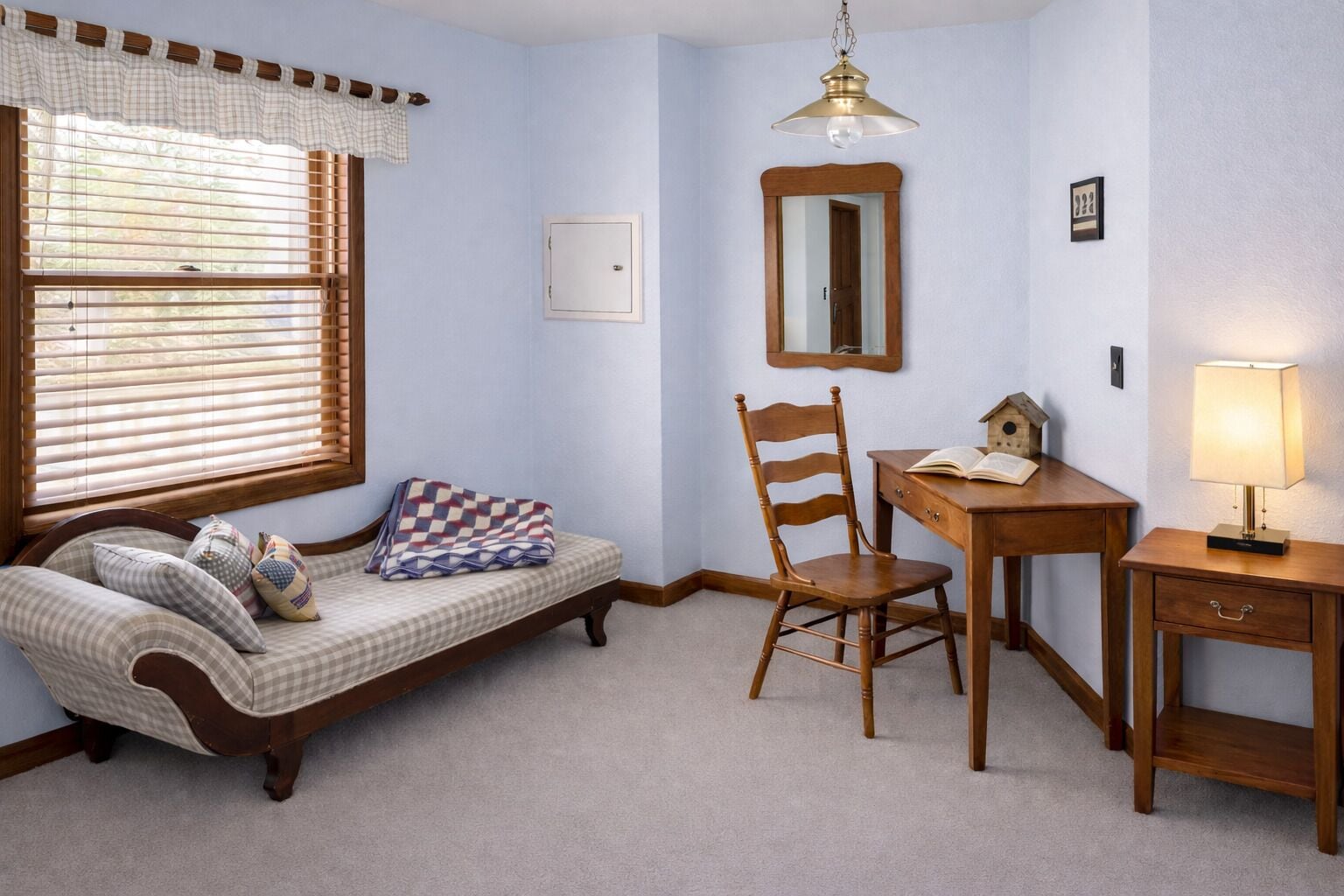 Una habitación con un sofá estampado, una silla de madera, escritorio, lámpara y un candelabro colgante.