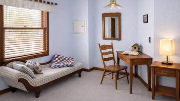 Una habitación con un sofá estampado, una silla de madera, escritorio, lámpara y un candelabro colgante.
