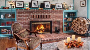 Un salon chaleureux avec une cheminée en briques, un fauteuil à motifs, des étagères et une table ronde décorée de bougies.