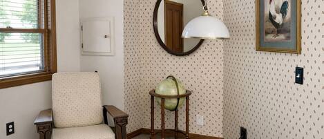 A room with a wooden chair, a globe on a stand, a mirror, and a rooster painting.