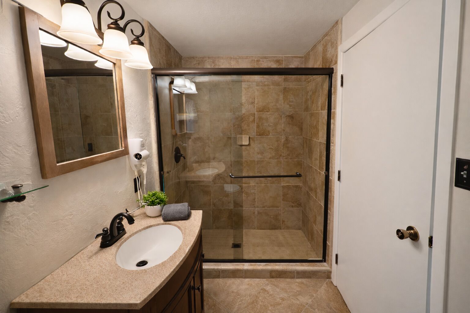 A bathroom with a glass shower enclosure, a sink with a mirror above it, and a towel rack.