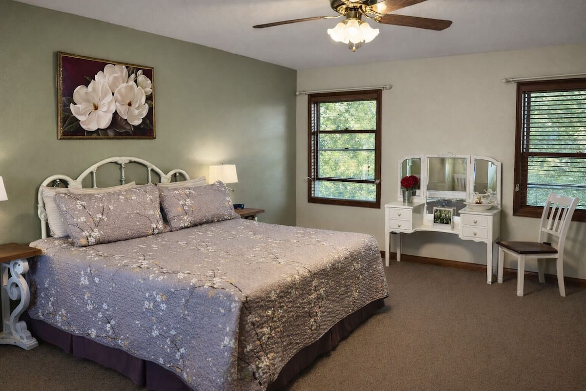 A bedroom with a bed, dresser, vanity, and a ceiling fan.