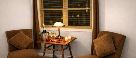Una habitación de esquina con dos sillones de cuero marrón, una pequeña mesa de madera con una lámpara, una botella de champán, copas y una vela encendida.