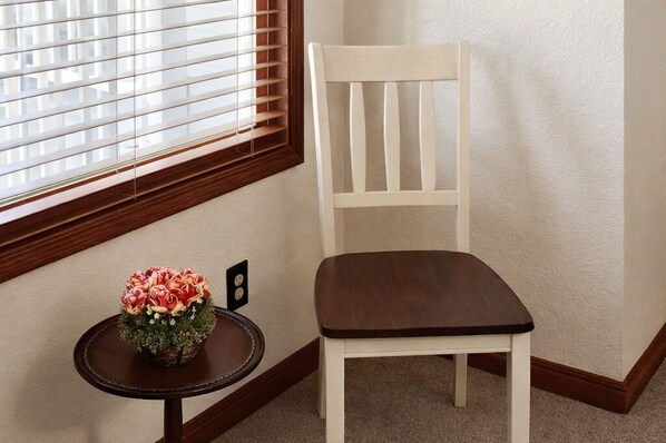 A corner room with a white chair, a small round table with a floral arrangement, and a window with blinds. - The Bidwell House (Chester)