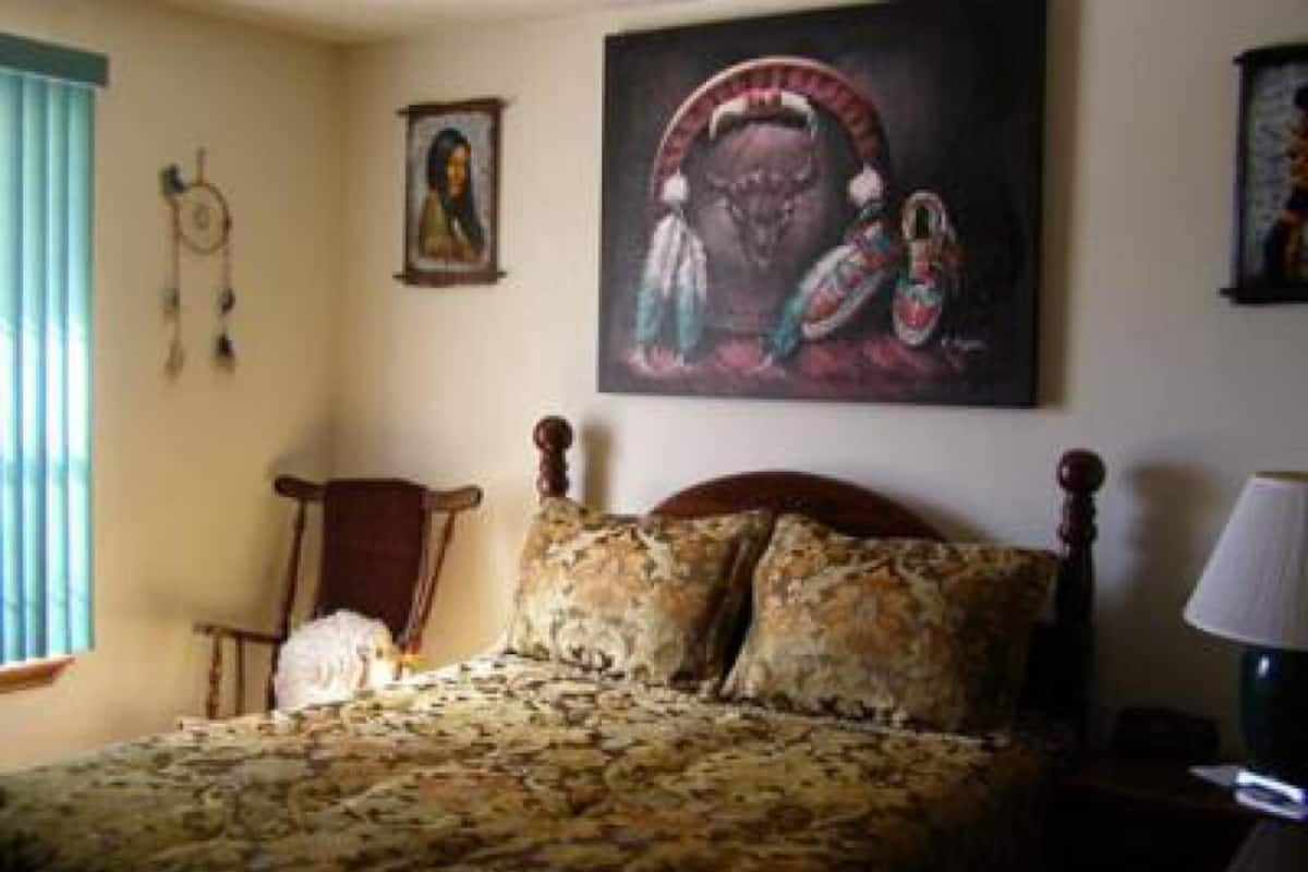 Une chambre à coucher avec un lit, une chaise, une lampe et un tableau au mur.