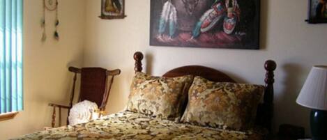 A bedroom with a patterned bedspread, a wooden headboard, a dreamcatcher, and a painting of a bull and feathers on the wall.