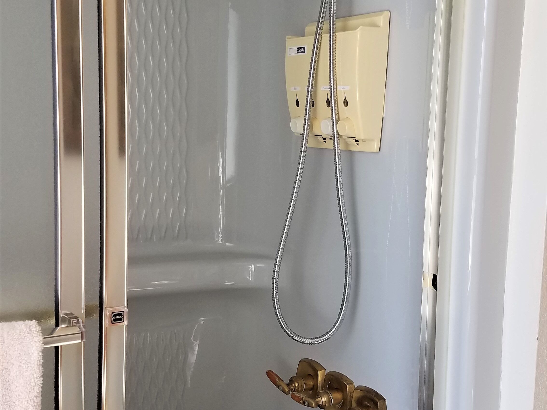 A shower area with a handheld showerhead and a wall-mounted control panel.