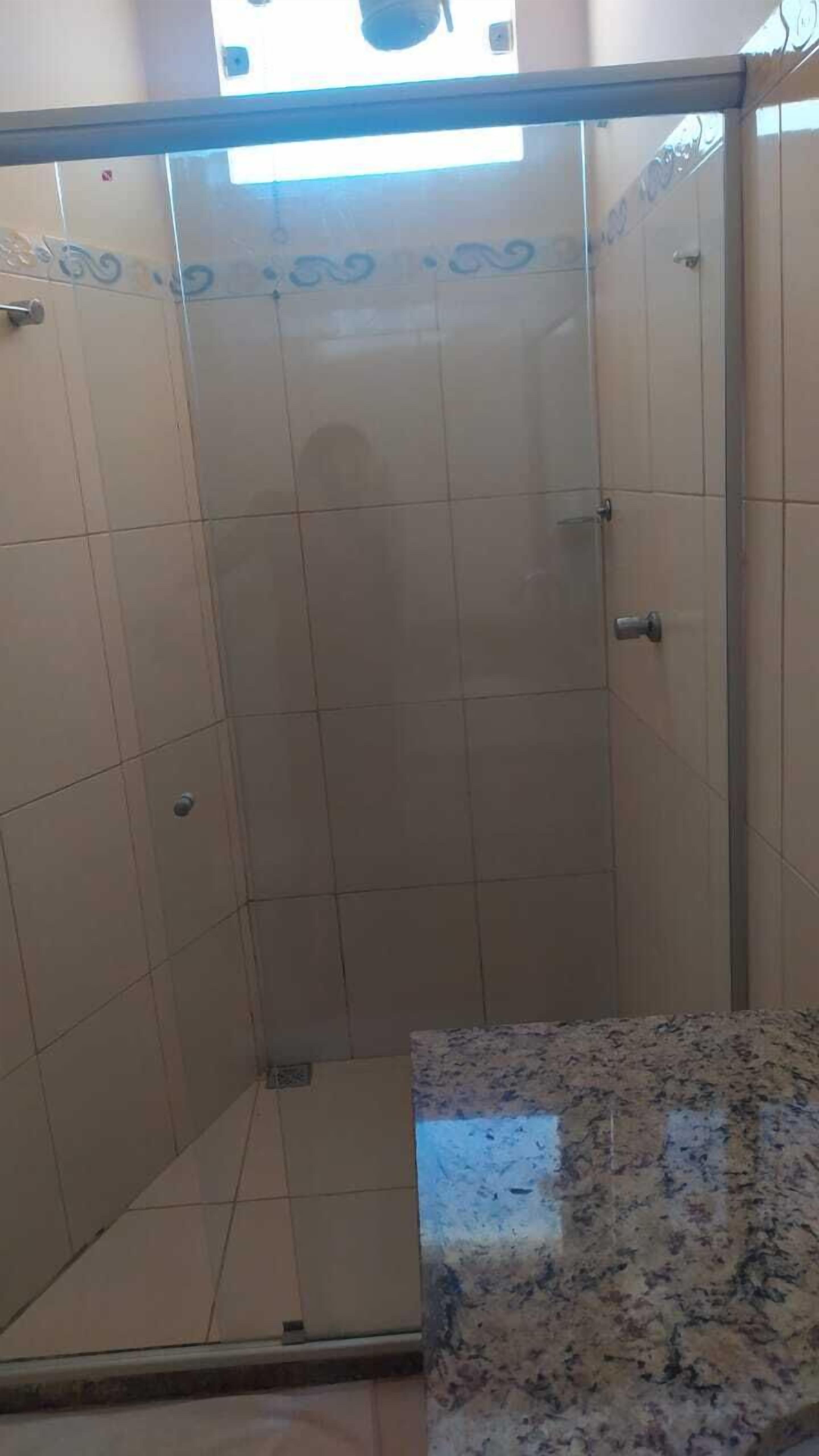 Um box de chuveiro revestido com azulejos, piso em azulejo e bancada de granito.