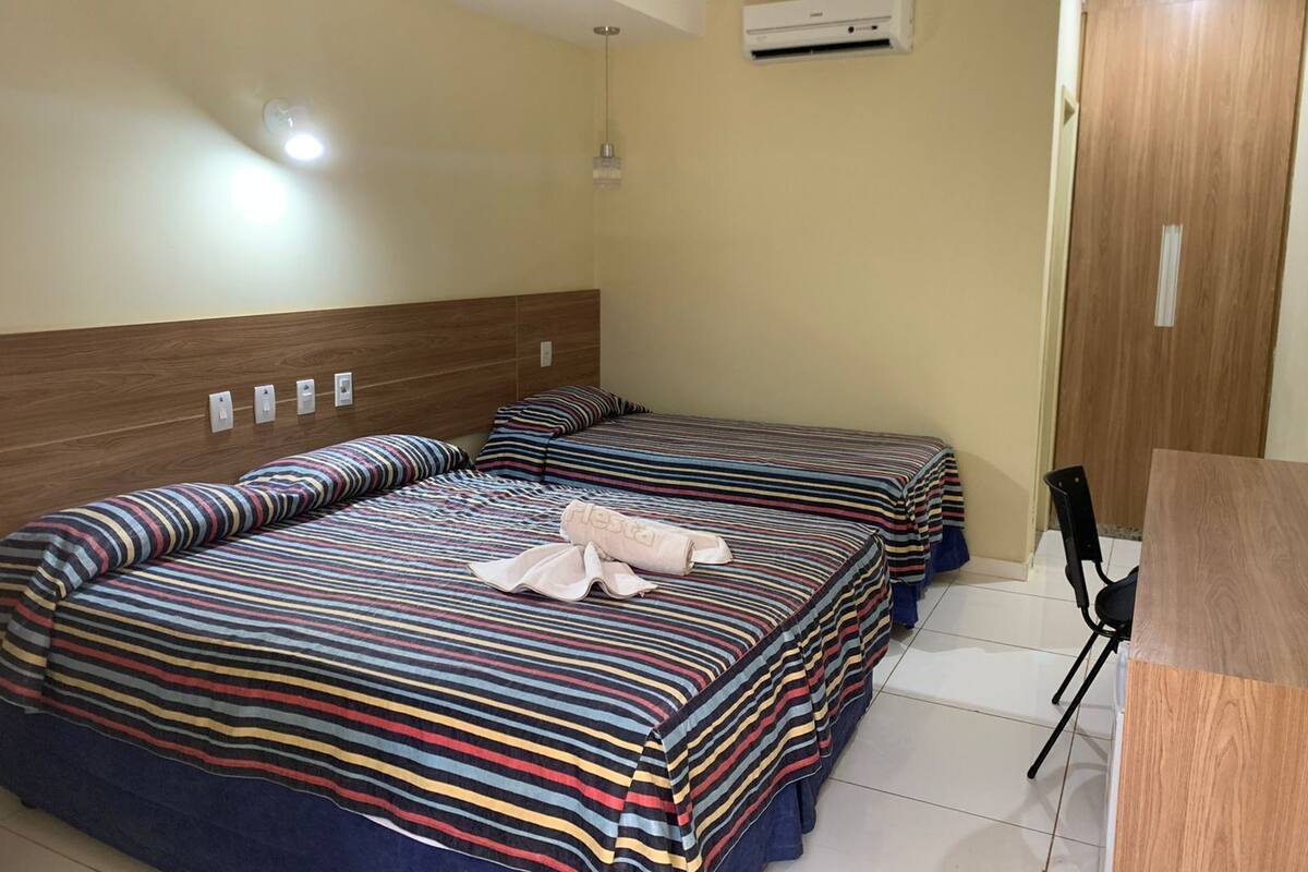 Habitación de hotel con dos camas, cabecero de madera, unidad de aire acondicionado y puerta de madera.