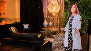 Un interior moderno con un sofá de cuero negro, cojines decorativos, una planta grande y una araña.