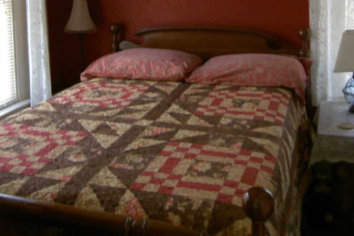 A bedroom with a bed, a lamp, a painting, and curtains.