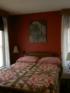 A bedroom with a bed, a lamp, a painting, and curtains. - Gallagher's Irish Rose (Red Lodge)