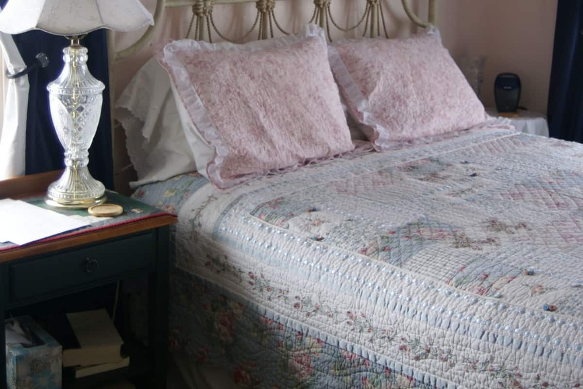 A bedroom with a bed, a nightstand, a lamp, a framed picture on the wall, and a window with curtains.