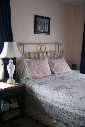 A bedroom with a bed, a nightstand, a lamp, a framed picture on the wall, and a window with curtains. - Gallagher's Irish Rose (Red Lodge)