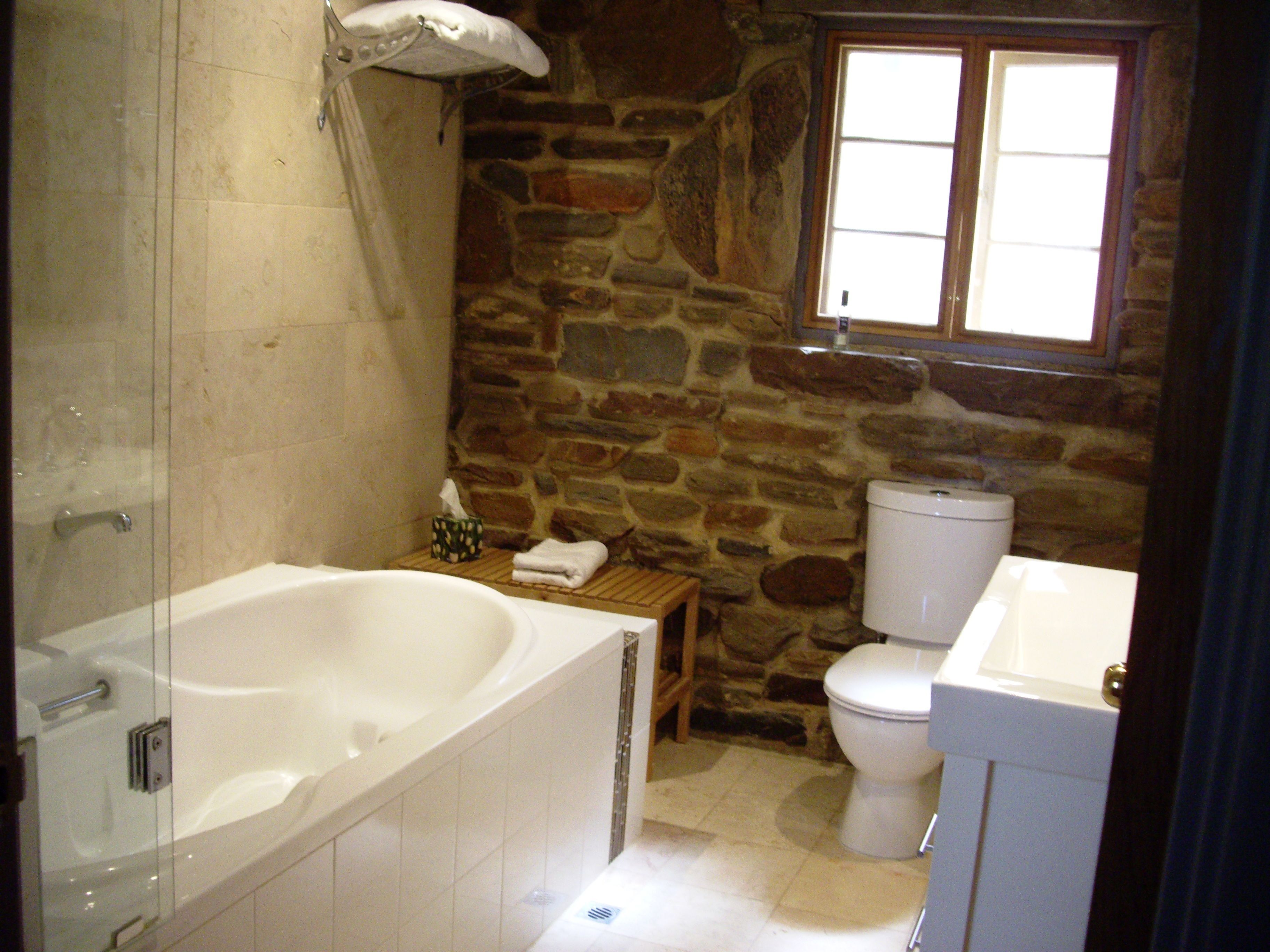A bathroom with a stone wall, a bathtub, a toilet, and a window.
