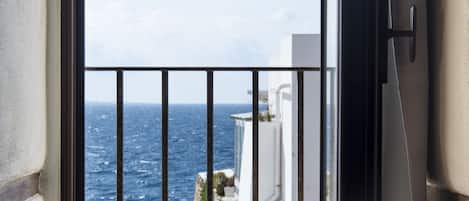 A balcony with a view of the sea and a building across the water.