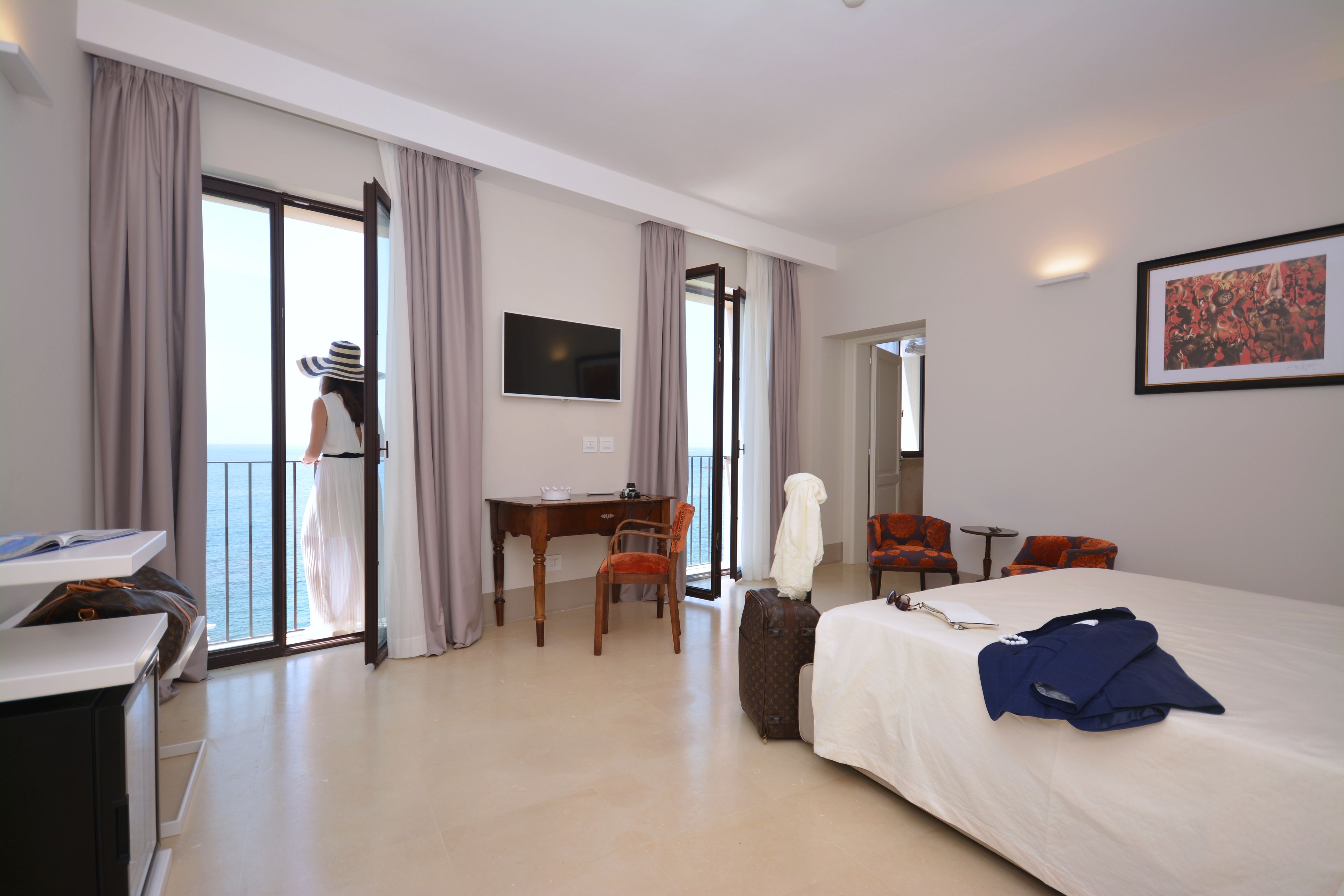 Een hotelkamer met een bed, een bureau, een stoel, een televisie en uitzicht op zee.