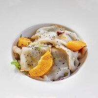 Un plato de comida con filetes finos de pescado, gajos de naranja y semillas de sésamo negro.