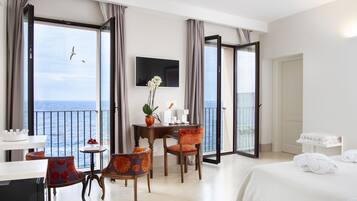 A hotel room with a balcony, a dining area, a TV, and a bed with towels.