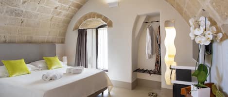 A bedroom with a bed, pillows, a bedside table, a plant, and a mirror.