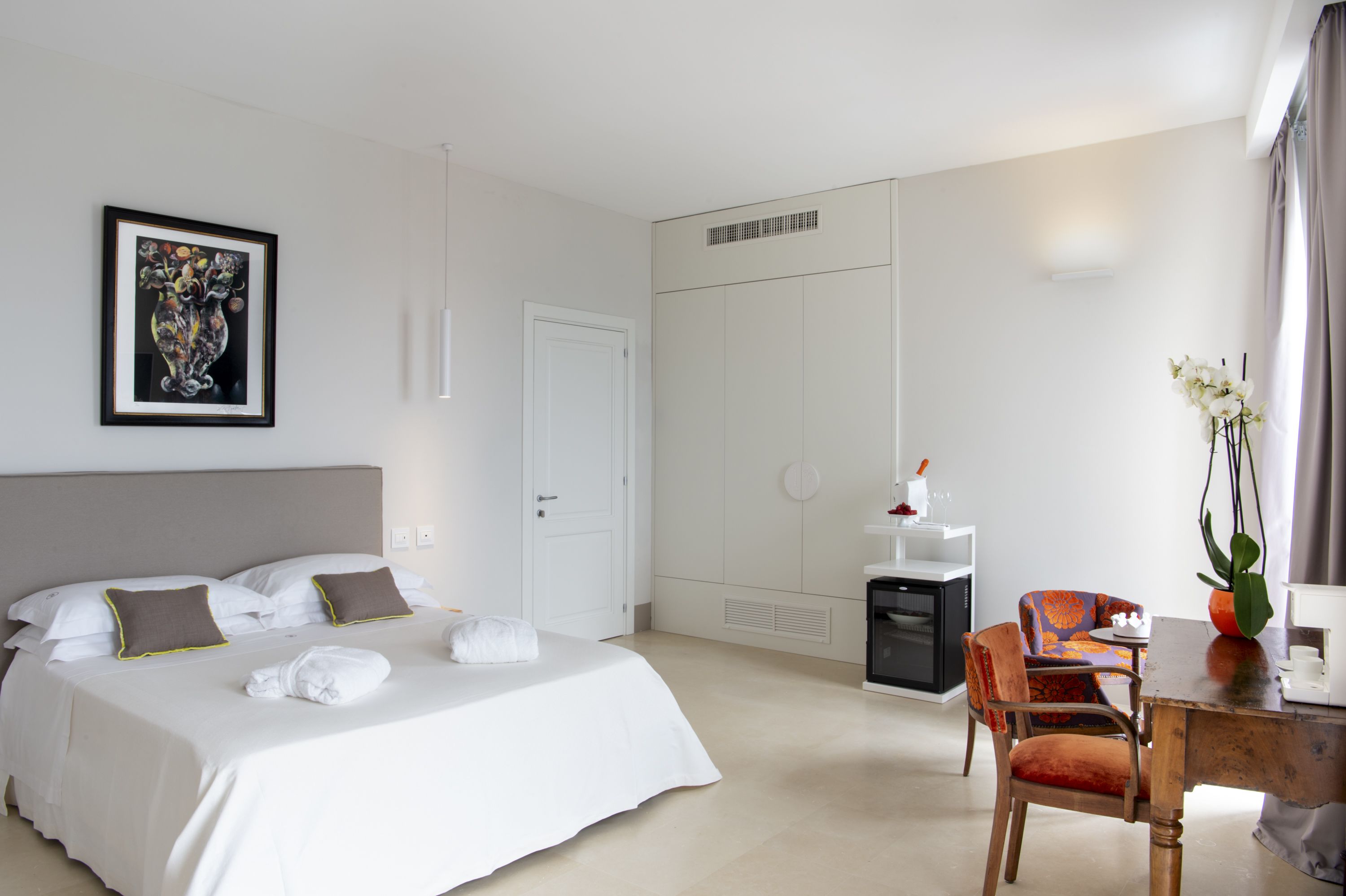 Une chambre d’hôtel avec un lit, un bureau, une chaise, une petite table, une plante et un tableau encadré au mur.