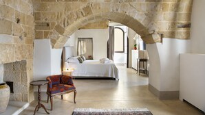 Une chambre avec une arche en pierre, un lit, une chaise et une table de chevet.