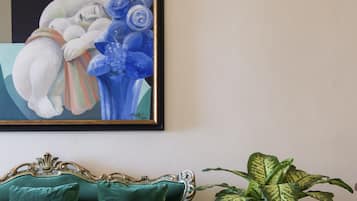 A room with a green sofa, a framed painting, and a potted plant.
