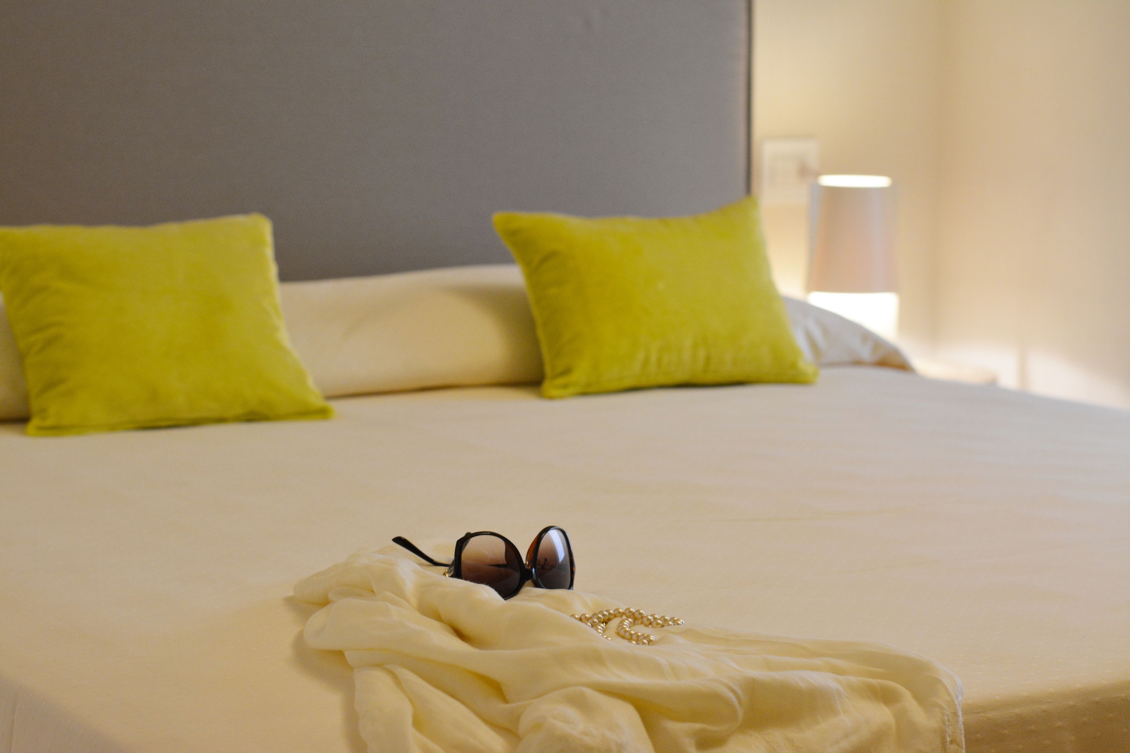 A neatly made bed with a white comforter, two bright green pillows, and a pair of sunglasses on the comforter.