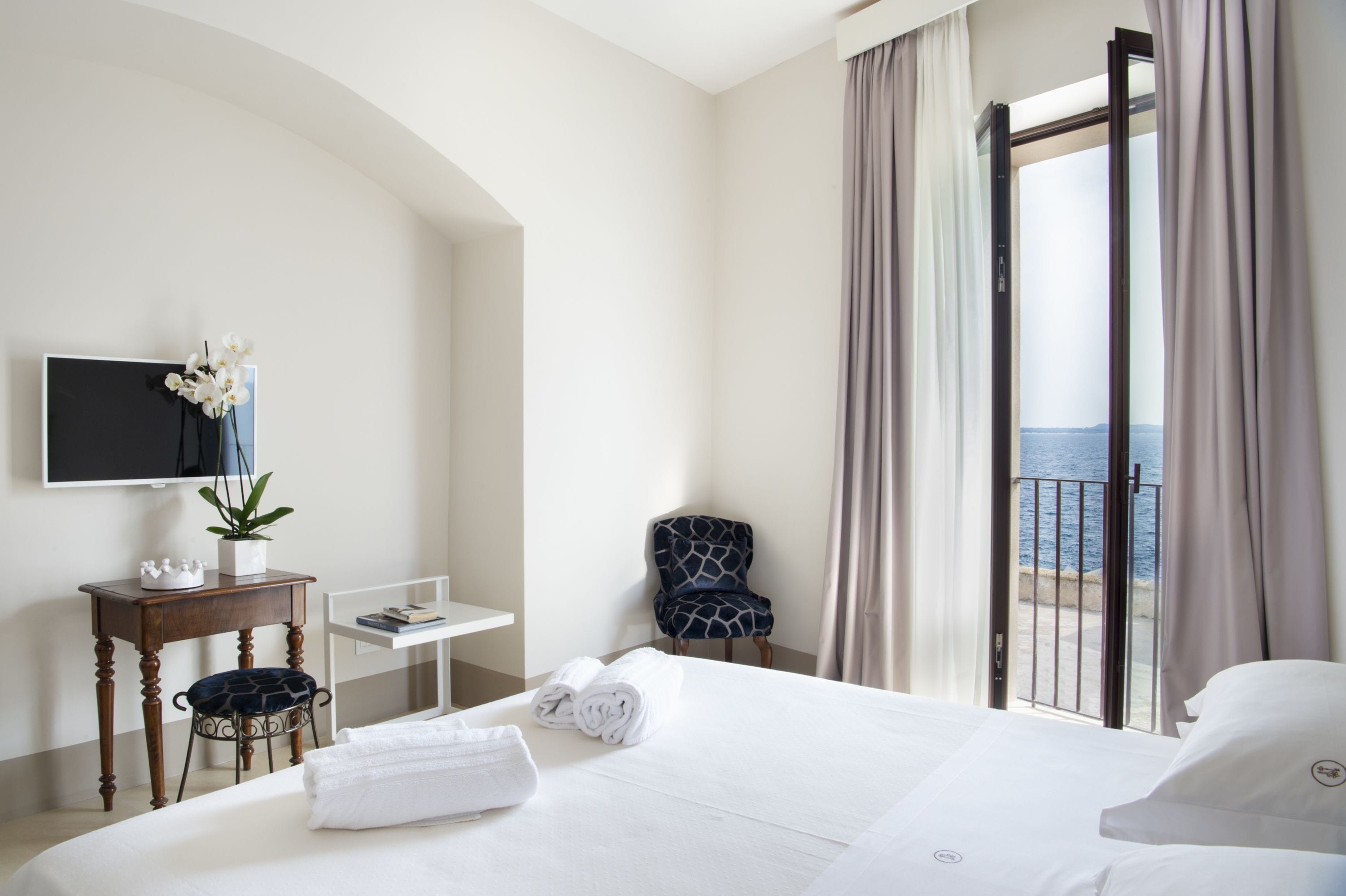 Een hotelkamer met een bed, een bureau, een stoel, een televisie en uitzicht op zee.