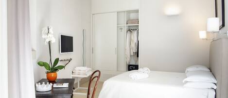 A hotel room with a bed, a desk with a chair, a potted plant, a TV, and a closet.