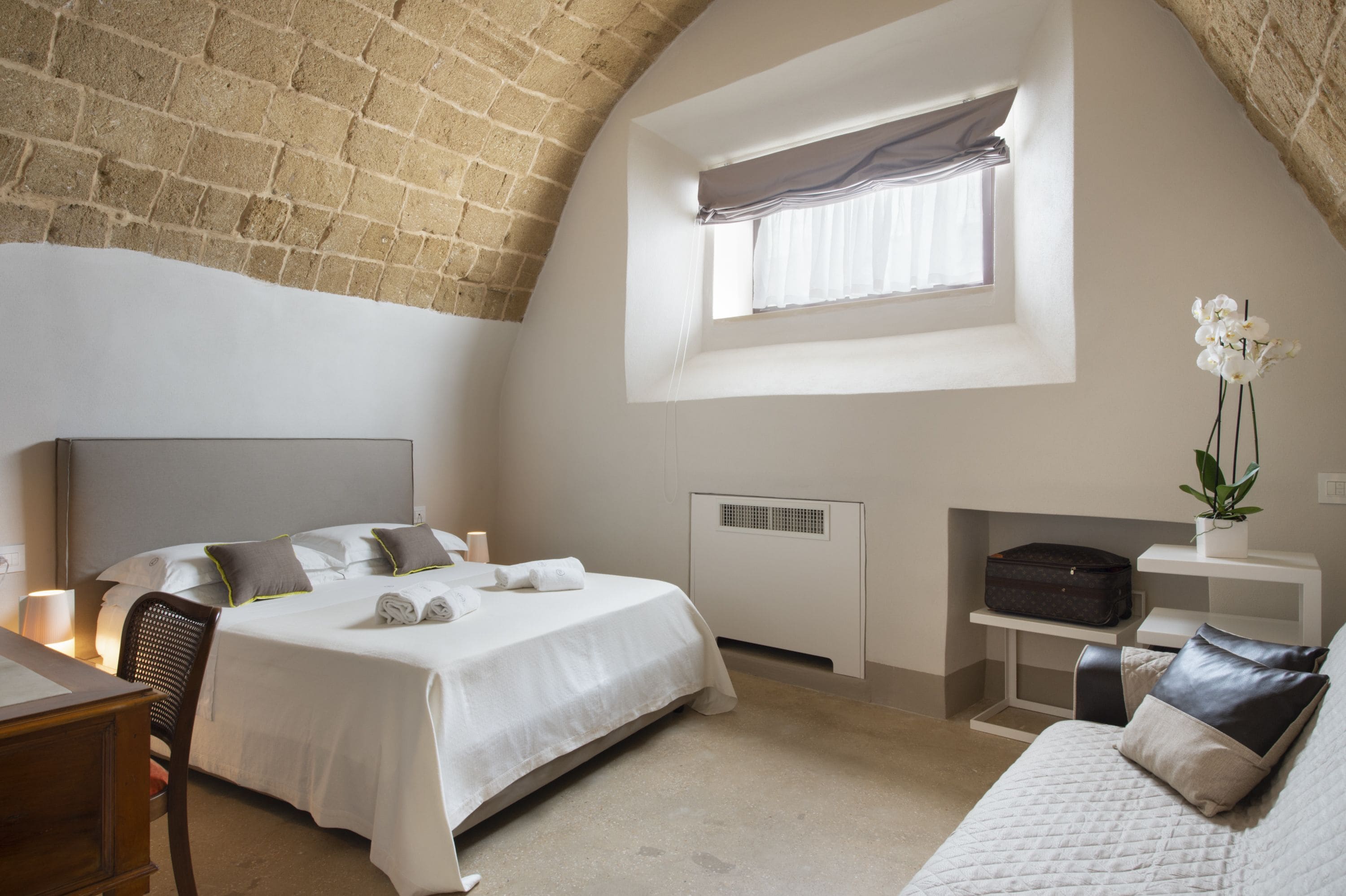 Un dormitorio con cama, escritorio, silla, ventana y planta.