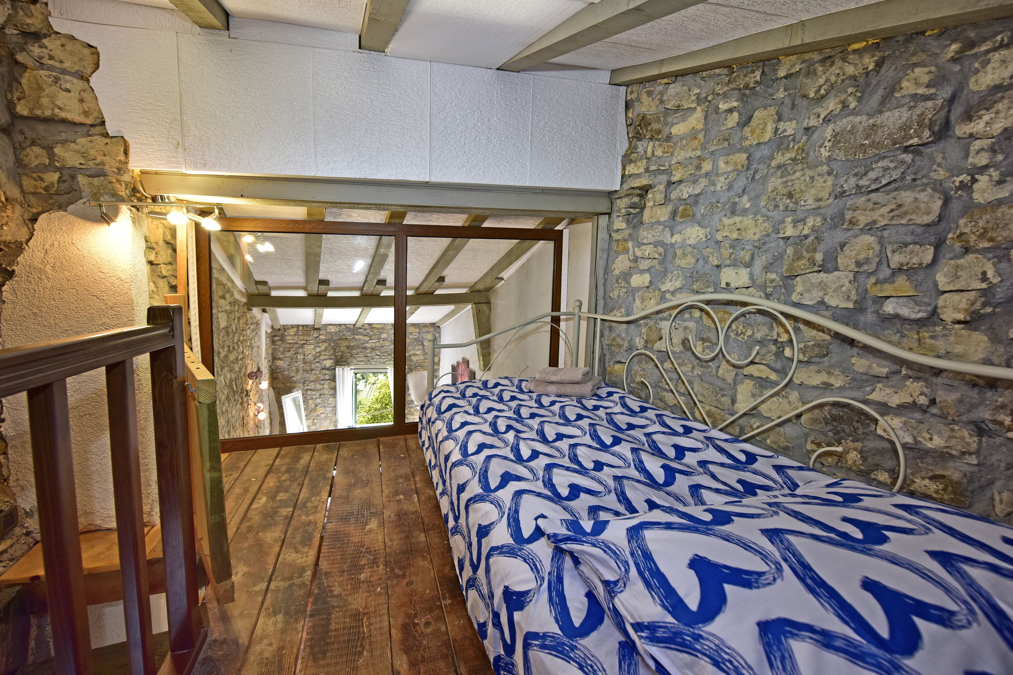 Ein Schlafzimmer mit Holzboden, einem Bett mit gemustertem Überwurf, einer Steinwand und einer Holztreppe.