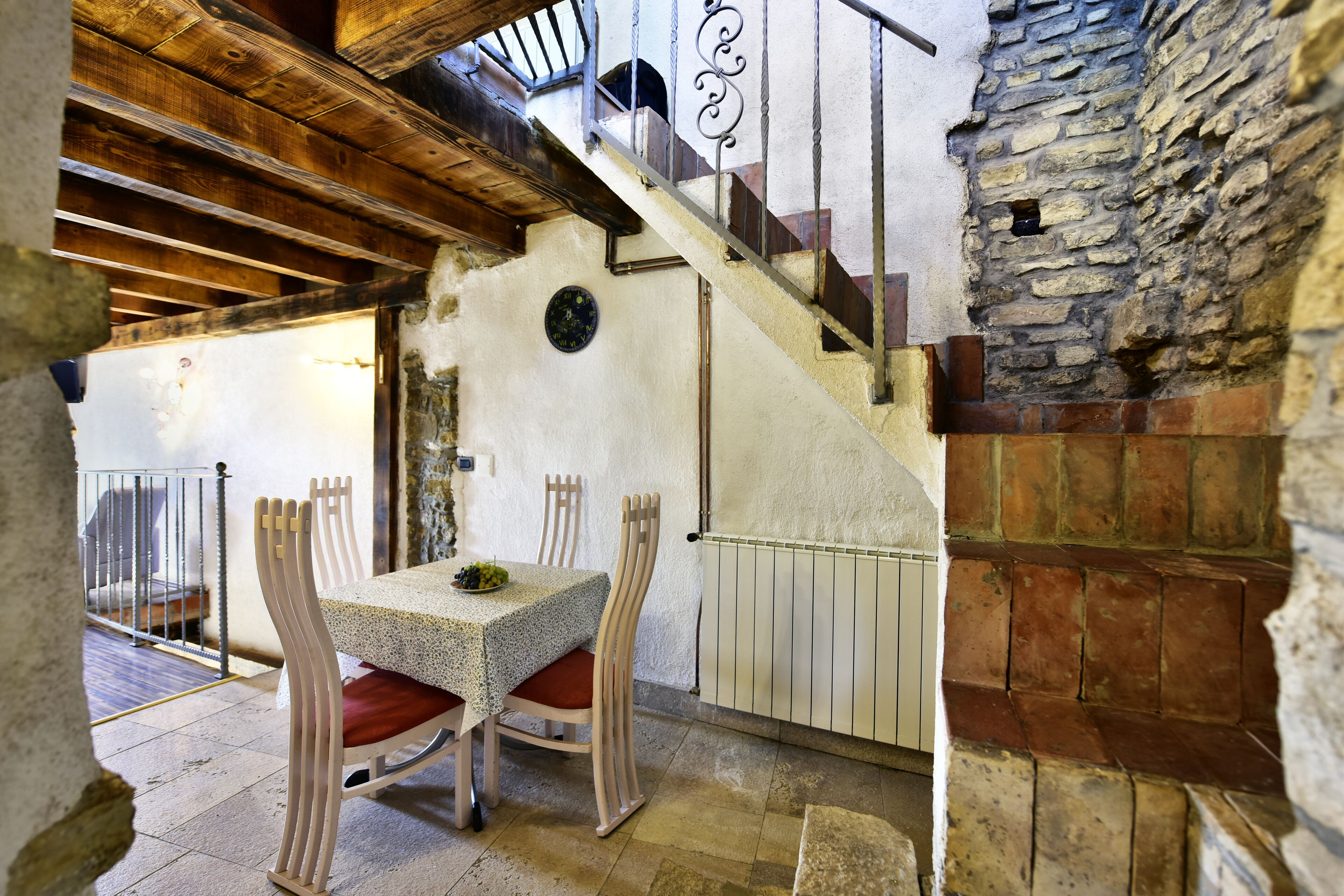 A rustic dining area with a table and chairs, a staircase, and a stone wall.