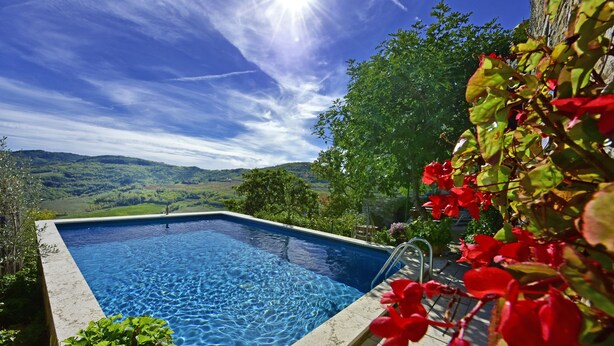 Una piscina rectangular con agua azul cristalina, rodeada de vegetación y vistas a colinas distantes.