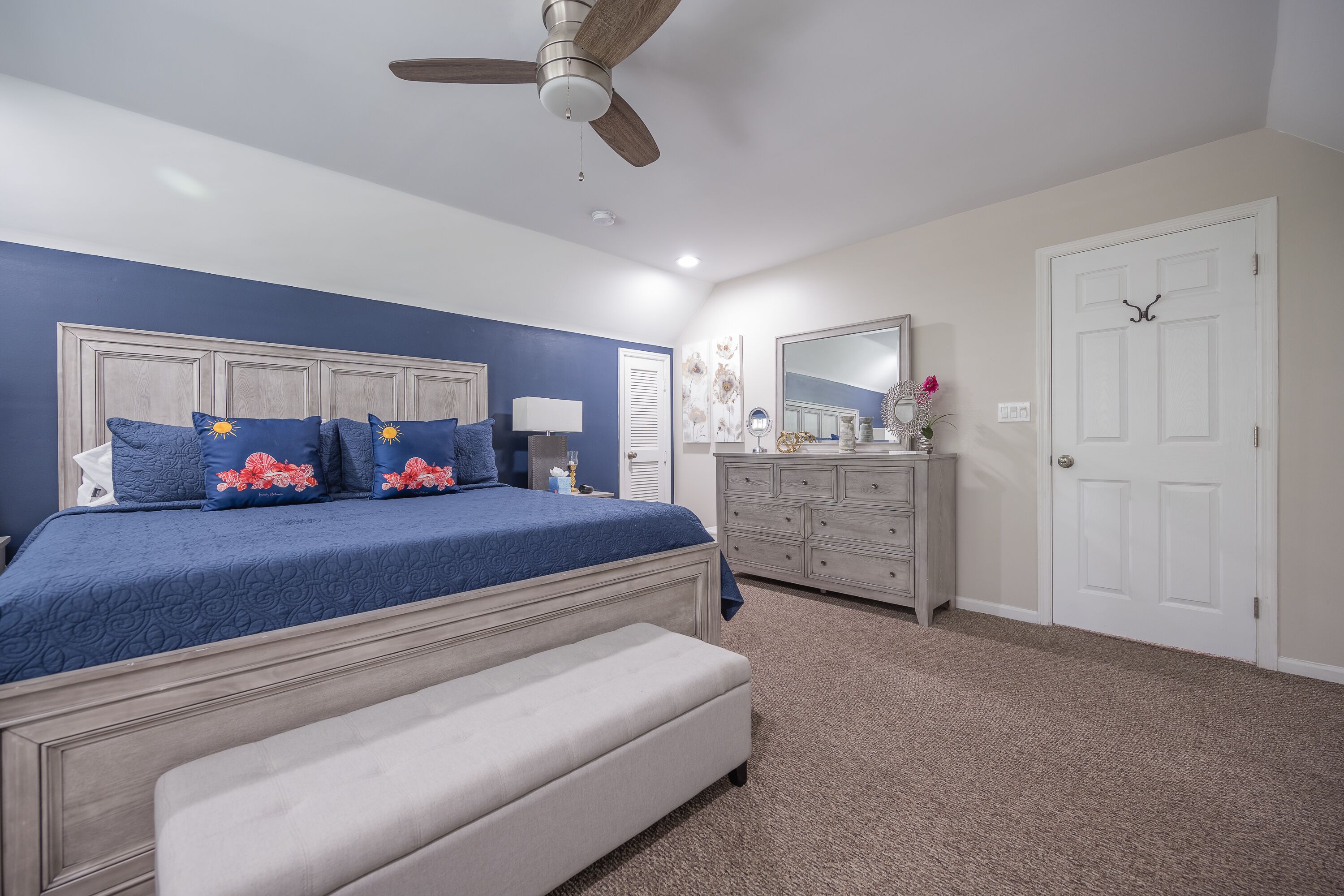 A bedroom with a bed, a bench, a dresser, a mirror, and a ceiling fan.