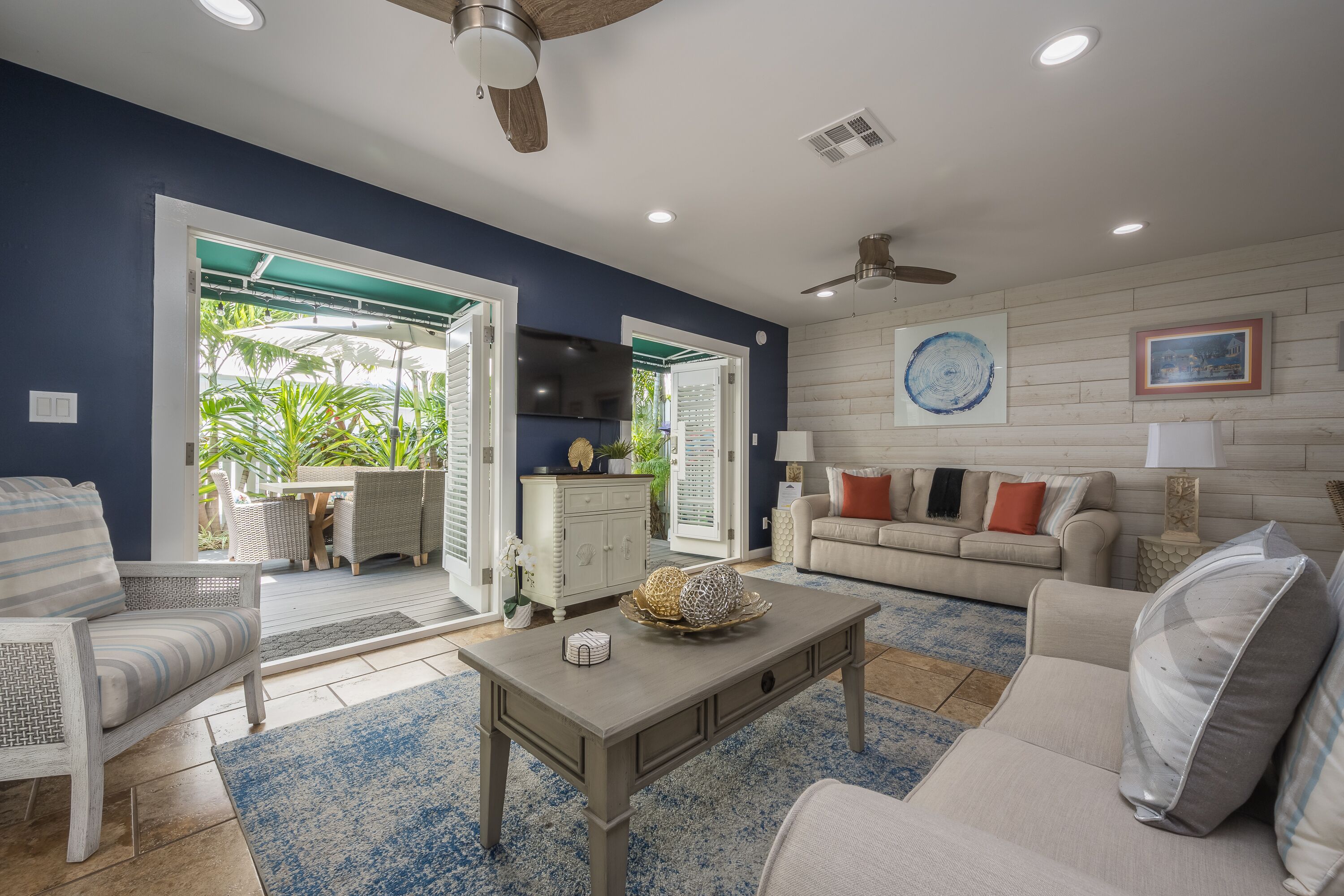 A spacious living room with a large window, a ceiling fan, and a dining area with outdoor seating.