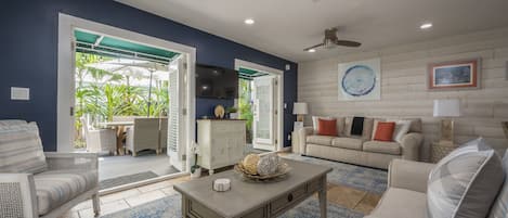A spacious living room with a large window, a ceiling fan, and a dining area with outdoor seating.