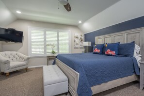 A bedroom with a bed, a chair, a bench, a TV, a window with blinds, and artwork on the wall. - Blue Lagoon at The Truman Annex in Key West (Key West)
