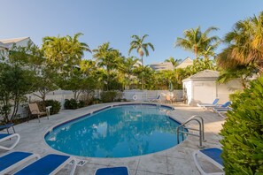 A swimming pool with blue and white lounge chairs, surrounded by palm trees and a white fence. - Blue Lagoon at The Truman Annex in Key West (Key West)