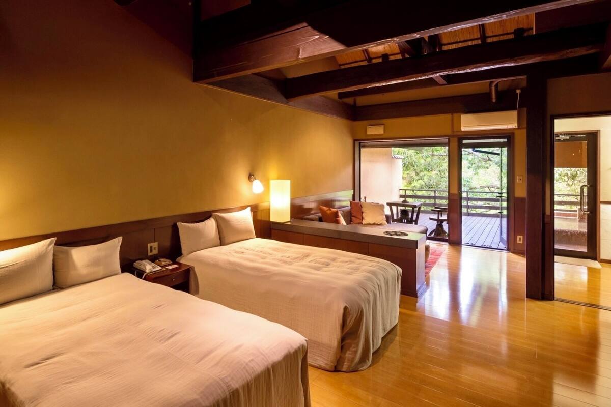 A hotel room with two beds, a small seating area, and a view of the outdoors.