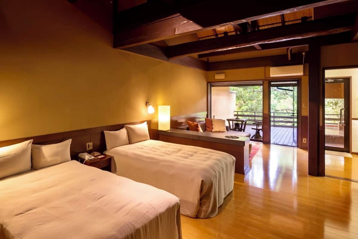 A hotel room with two beds, a small seating area, and a view of the outdoors.