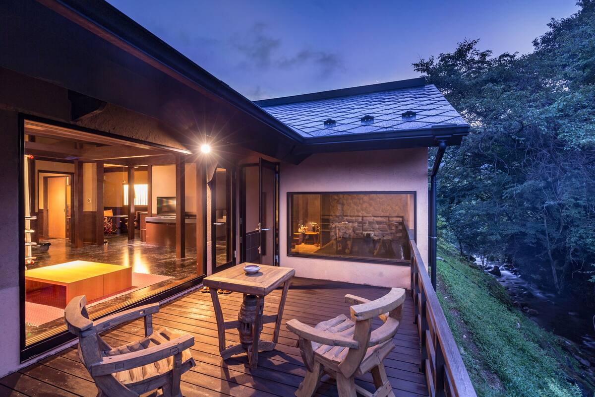 A modern house with a wooden deck, large windows, and a view of a river.