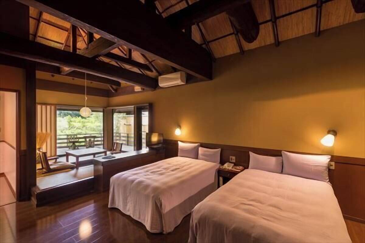 A hotel room with two beds, a wooden ceiling, a window with a view, and a table with chairs.