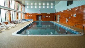 An indoor swimming pool with lounge chairs, a wooden wall, and a ceiling with a grid pattern.